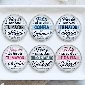 Puede incluir: Seis pines circulares con bordes metálicos que presentan textos religiosos en español. La fila superior incluye texto en azul y gris, mientras que la fila inferior muestra texto en rosa y gris. Cada pin exhibe frases como Haz de Jehová tu mayor alegría y Feliz es el que confía en Jehová con pequeños detalles de corazones y hojas.