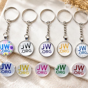 Puede incluir: Una colección de cinco llaveros circulares con anillas y cadenas de metal plateado, cada uno con el texto JW.ORG en varios colores y patrones, junto con cinco pines circulares a juego con el texto JW.ORG en color.