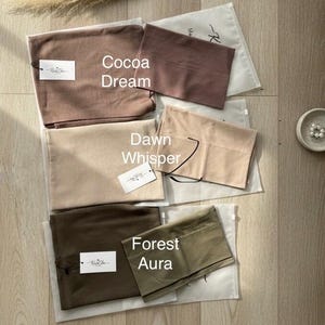 May include: A collection of rectangular fabric pieces in shades of brown, beige, and olive green, labelled Cocoa Dream, Dawn Whisper, and Forest Aura. Each piece is packaged in a translucent plastic sleeve with a white tag featuring the KnitChe logo.