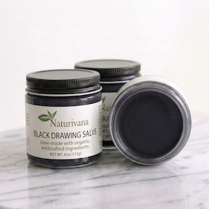 Puede incluir: Dos frascos de vidrio con tapas negras que contienen ungüento negro. La etiqueta dice Naturivana Black Drawing Salve, slow-made with organic, wildcrafted ingredients, NET WT. 4 oz (113g). Un frasco está vertical, el otro está inclinado para mostrar el ungüento.