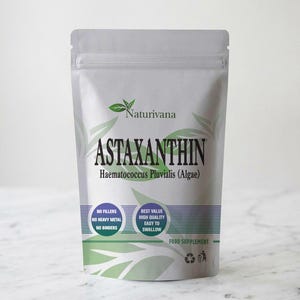 May include: A silver stand-up pouch of Naturivana Astaxanthin food supplement. The label features green leaf graphics, the text "ASTAXANTHIN Haematococcus Pluvialis (Algae)", and circular badges stating "No Fillers, No Heavy Metal, No Binders" and "Best Value, High Quality, Easy to Swallow".