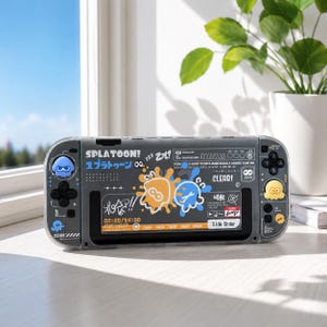 Peut inclure: Une console de jeu portable dotée d'une coque de protection gris translucide avec des graphismes sur le thème de Splatoon. Le design inclut des taches d'encre orange et bleue, du texte japonais, le mot CLEAR! et de petites icônes de calmar. Des capuchons de joystick en forme de calmar jaune et bleu sont fixés.