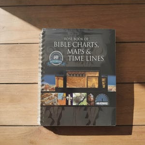 Può includere: Un libro con rilegatura a spirale intitolato Rose Book of Bible Charts, Maps & Time Lines con una copertina scura che presenta un badge best seller del decimo anniversario, un'illustrazione architettonica centrale e immagini storiche.