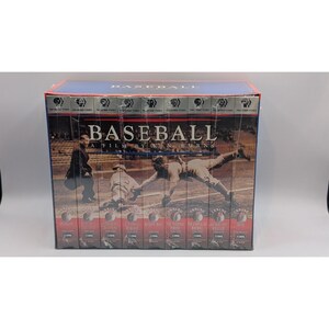 May include: A boxed set of VHS tapes titled Baseball: A Film by Ken Burns. The box features a sepia-toned photograph of baseball players on a field. The text Baseball: A Film by Ken Burns is printed in white across the centre of the box set.