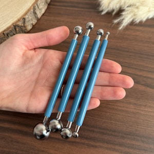 Könnte beinhalten: Ein Set aus vier doppelseitigen Kugel-Stylus-Werkzeugen mit glatten, hellblauen zylindrischen Griffen und polierten silberfarbenen Metallkugeln in verschiedenen Größen an jedem Ende, konzipiert für präzises Basteln, Modellieren und Detailarbeiten.