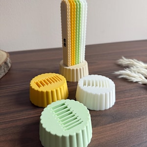 Può includere: Una pila verticale di quattro sottili pannelli rettangolari con bordi smerlati in crema, giallo, verde chiaro e bianco, montati su una base circolare. Tre basi circolari smerlate aggiuntive in giallo, bianco e verde chiaro sono posizionate davanti.