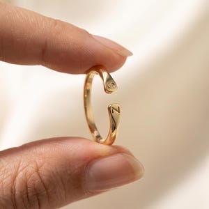 May include: A gold-toned open ring featuring a polished finish with the letter S engraved on the top terminal and the letter Z engraved on the bottom terminal. The band is slender and circular, designed with a gap between the two ends.