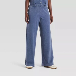 Könnte beinhalten: Weit geschnittene Hose in verwaschenem Blau mit hoch sitzendem, elastischem Bund und einem sichtbaren Knopfverschluss in der Mitte. Die Hose hat eine lockere, gerade Beinform, die bis zu den Knöcheln reicht und eine gleichmäßige Textur aufweist.