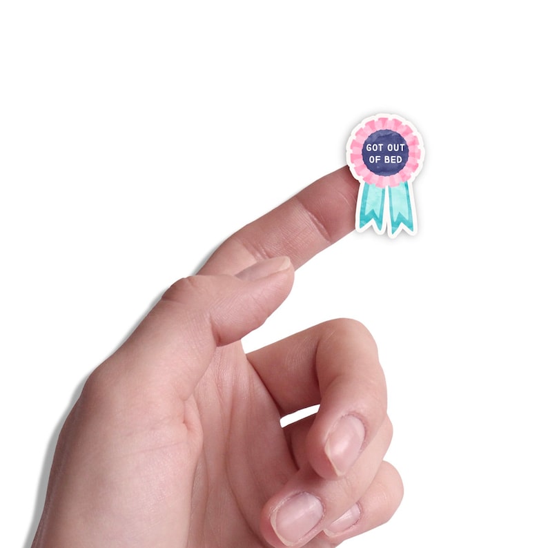 May include: A pink and blue watercolor sticker with a white ribbon and the text "GOT OUT OF BED".