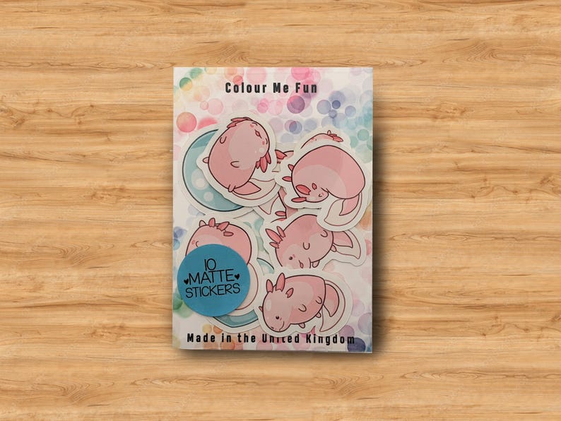 May include: A sheet of 10 matte stickers featuring pink axolotl illustrations. The stickers are on a white background with a rainbow pattern and the text "Colour Me Fun". The sheet also includes the text "10 Matte Stickers" and "Made in the United Kingdom".