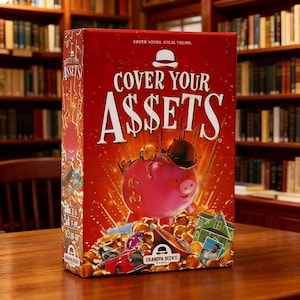 May include: A rectangular board game box titled Cover Your Assets with a red background. The front features a pink piggy bank wearing a black bowler hat, surrounded by gold coins, a red car, a house, and a portrait. Text reads Cover Your Assets.