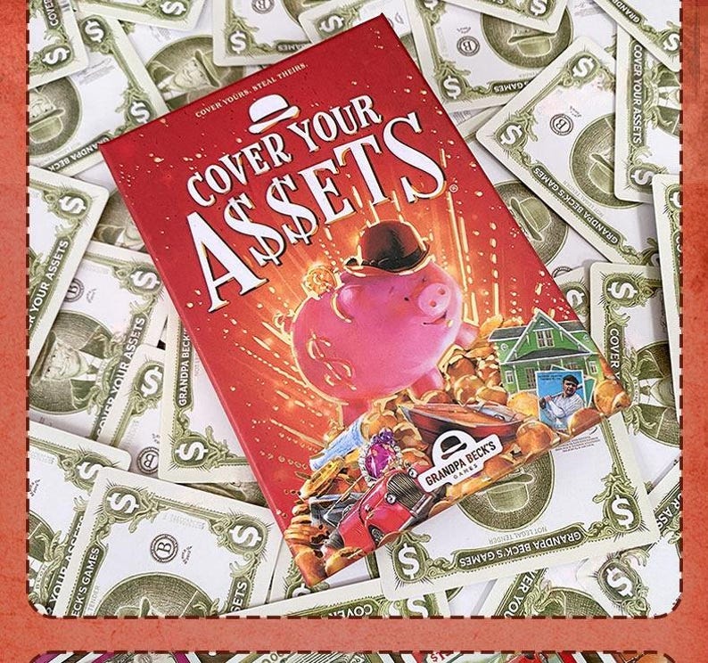 May include: The Cover Your Assets card game box features a red background with a pink piggy bank wearing a black bowler hat, surrounded by gold coins, a house, and a car. The text reads Cover Your Assets and Grandpa Beck's Games.