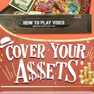 May include: A board game box titled Cover Your Assets with a red background, white lettering, and a graphic of gold coin stacks. The box lid features a black metal-style panel with the text HOW TO PLAY VIDEO and the URL gbecks.com/cya-vid.