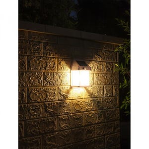 May include: A rectangular solar-powered wall light mounted on a textured brick surface. The fixture features a white translucent panel emitting a warm, bright glow, with a small solar panel and a motion sensor integrated into the top housing.