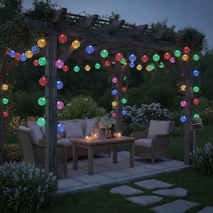 Op de afbeelding: Een lichtsnoer met veelkleurige led-bollen gedrapeerd over een houten pergola. De lampen hebben bolvormige, getextureerde kappen die oplichten in diverse kleuren, waaronder rood, blauw, groen, geel en roze, en verlichten de buitenruimte op het terras.