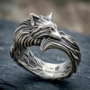 May include: A silver-toned ring shaped like a wolf with detailed fur texture. The wolf's head and tail meet to form the band. The interior of the ring is engraved with the text .925, a paw print icon, and the words FOREST WOLF in capital letters.