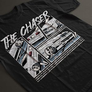 May include: A black short-sleeved t-shirt featuring a graphic print with the text THE CHASER in a bold white font. The design includes three separate panels showing illustrations of a white sedan from different angles and Japanese text.