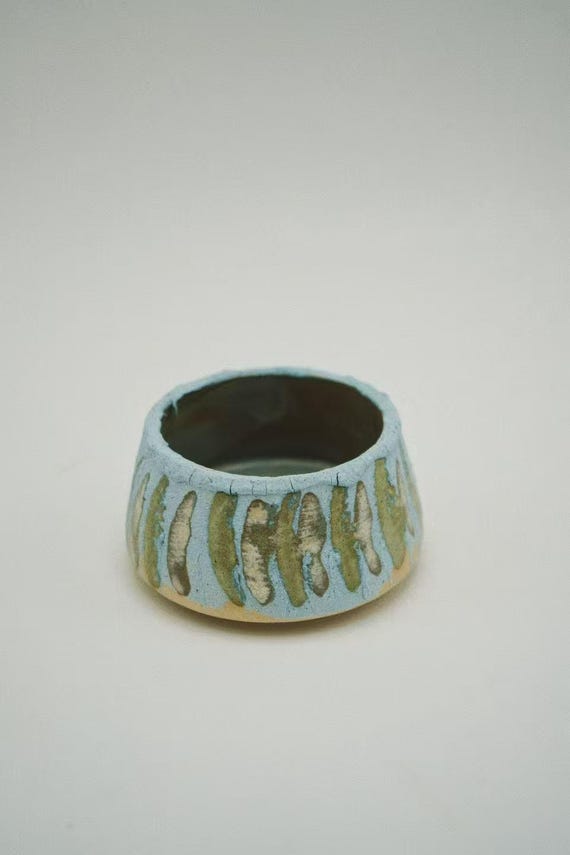 A wheel-thrown, hand-carved stoneware sake/tea cup with a wabi-sabi blue-green glaze — the kind of imperfect, tactile object you pick up and don't want to put down.
