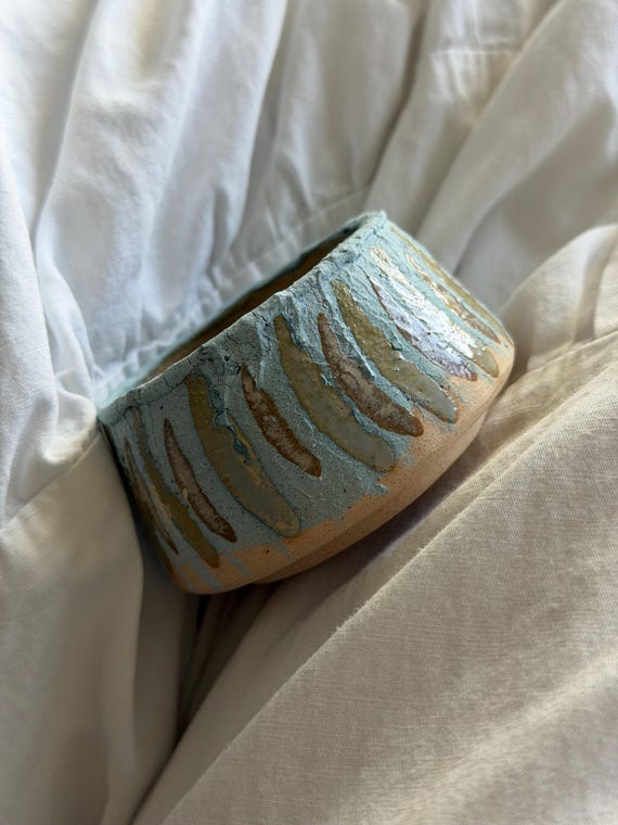 A wheel-thrown, hand-carved stoneware sake/tea cup with a wabi-sabi blue-green glaze — the kind of imperfect, tactile object you pick up and don't want to put down.