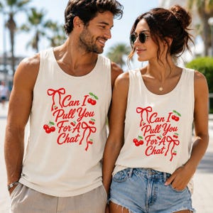 May include: Two matching cream-colored tank tops featuring red text that reads Can I Pull You For A Chat, accented with red cherry illustrations and red ribbon graphics. The sleeveless shirts have a round neckline and a simple, casual design.
