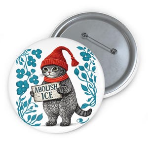 May include: A round pin-back button featuring a black and white illustration of a cat wearing a red knit hat and scarf. The cat holds a sign that reads ABOLISH ICE. The design is framed by blue floral vines on a white background.
