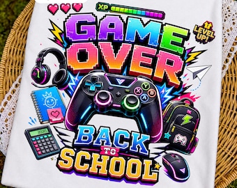 Op de afbeelding: Een wit t-shirt met een kleurrijke afbeelding en de tekst GAME OVER BACK TO SCHOOL. Het ontwerp bevat een zwarte gamecontroller, een koptelefoon, een rekenmachine, een rugzak, een computermuis, een notitieboek en een level up icoon.