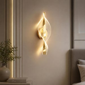 May include: A wall-mounted light fixture featuring a vertical gold metal centre spine with two curved, translucent acrylic panels that spiral outward. The panels have a textured, speckled finish and emit a warm, glowing light from within.