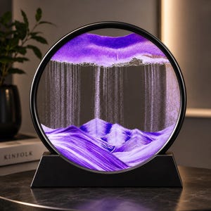 May include: A circular sand art display featuring a black frame and base. Inside the glass, purple sand creates a layered mountain landscape at the bottom, while fine streams of sand fall from a dense purple cloud formation at the top.