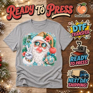 May include: A heather gray t-shirt featuring a graphic of Santa Claus wearing sunglasses with palm tree reflections, a straw hat, and a red hibiscus flower. Santa is blowing a pink bubble and making a peace sign, surrounded by tropical decor.