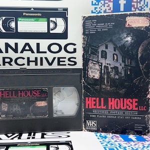 May include: A black VHS tape labeled Hell House LLC Recovered Footage Edition alongside its matching vertical cardboard slipcase. The cover features a dark, weathered house with the title in bold red text and the phrase Some Places Should Stay Off Camera.