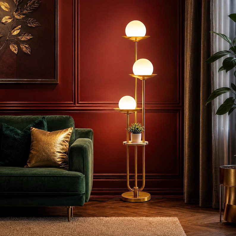 May include: A tall floor lamp with a gold-toned metal frame featuring three stacked tiers, each holding a spherical white glass light globe. A small circular shelf is integrated into the structure, supporting a potted green plant.