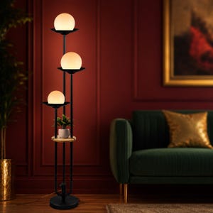May include: A black floor lamp featuring three vertical poles of varying heights, each topped with a white spherical glass shade. A small circular wooden shelf is integrated into the structure, holding a small green potted plant.