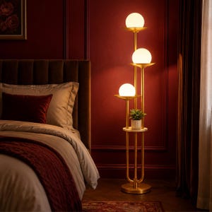 May include: A tall floor lamp with a gold-toned metal frame featuring three stacked white spherical glass shades, each resting on a circular tray. A small potted green plant sits on a circular shelf integrated into the lamp's vertical structure.