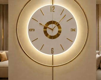 May include: A circular wall clock featuring a white face with gold-toned numerals at 12, 3, 6, and 9, surrounded by a thin gold metal ring. The clock includes a central gold circular accent, gold hands, and a vertical gold pendulum rod.
