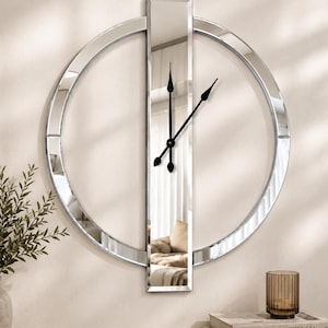 Peut inclure: Une horloge murale composée d'un cadre circulaire en miroir traversé par un panneau vertical rectangulaire en miroir. L'horloge possède trois fines aiguilles noires situées au centre du panneau vertical, reflétant l'intérieur de la pièce.