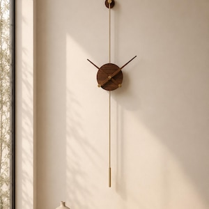 May include: A vertical wall clock featuring a circular dark wood center with two thin, dark wood hands. A long, slender brass rod extends vertically through the center, topped with a small circular wood accent and ending in a brass weight.