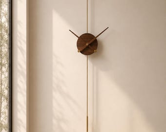 May include: A vertical wall clock featuring a circular dark wood center with two thin, dark wood hands. A long, slender brass rod extends vertically through the center, topped with a small circular wood accent and ending in a brass weight.