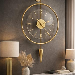 May include: A wall clock featuring a circular gold metal frame and a transparent center dial. The clock has gold-colored hands and numerals at the 12, 3, 6, and 9 positions. A vertical gold rod extends from the top mount to a pointed gold pendulum.