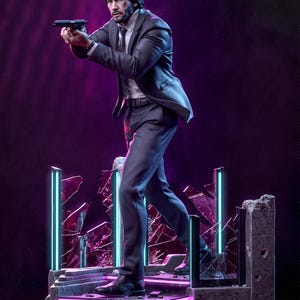 Può includere: Una dettagliata statuetta da collezione di un uomo con capelli scuri e barba, che indossa un abito scuro e una camicia bianca, mentre impugna una pistola nera. La figura poggia su una base in cemento rotto con barre luminose blu.