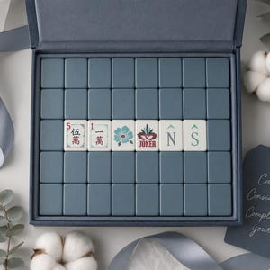 May include: A set of blue mahjong tiles arranged in a rectangular box. Six tiles in the center feature unique designs including Chinese characters, a blue flower, a red joker mask, and the letters N and S. A blue tag reads Calm. Considered. Completely yours.
