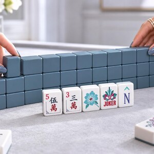 May include: A set of mahjong tiles featuring a row of solid slate blue tiles and a front row of white tiles with colorful printed designs including Chinese characters, a blue flower, a red and green joker symbol, and the letter N.