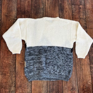 May include: A white and gray knitted sweater with a crew neck. The sweater is made of a soft, comfortable material and has a relaxed fit.
