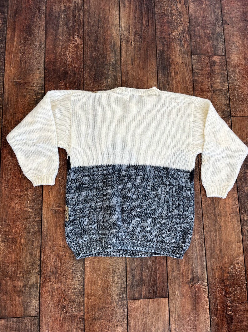 May include: A white and gray knitted sweater with a crew neck. The sweater is made of a soft, comfortable material and has a relaxed fit.
