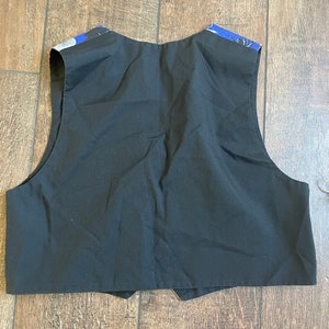May include: Black vest with a contrasting blue and white patterned fabric on the shoulders. The vest is made of a solid black material and has a classic, tailored design. The back of the vest is visible, showing the full shape and construction.