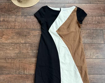May include: A short-sleeved dress with a color block design in black, white, and brown. A straw hat with a black band and a sprig of lavender are also visible.