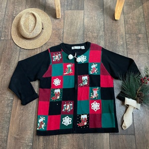 May include: Black zip-up cardigan with a red, green, and white checkered pattern. The cardigan features a festive design with embroidered Christmas stockings and snowflakes.