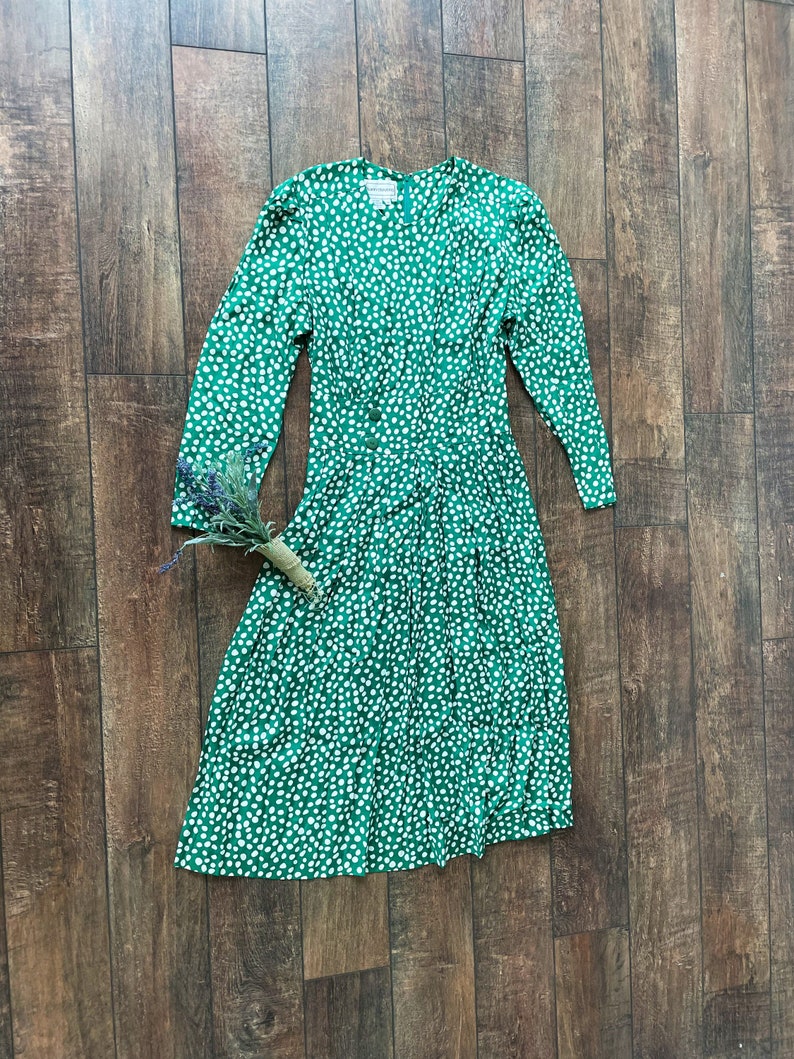 May include: A green dress with a white polka dot pattern. The dress has long sleeves and a button-up front.