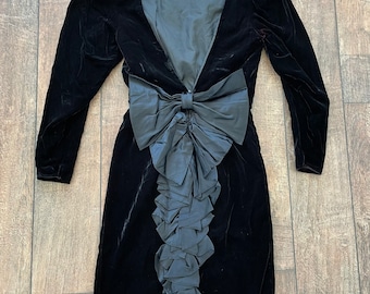 May include: A black velvet dress with a large bow and ruffle detail in the back.