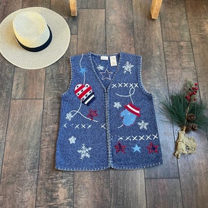 May include: A blue knitted vest with a zipper closure. The vest has a snowflake and star pattern and features red, white, and blue appliques of mittens and a snowman.