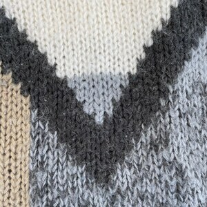 May include: Close-up of a knitted fabric with a geometric pattern in shades of beige, gray, and black.